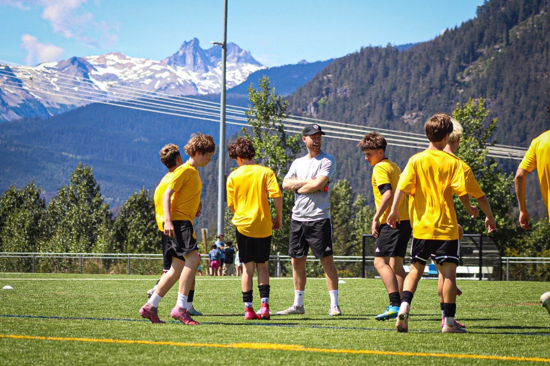 Players working with a coach, snow on the peaks behind