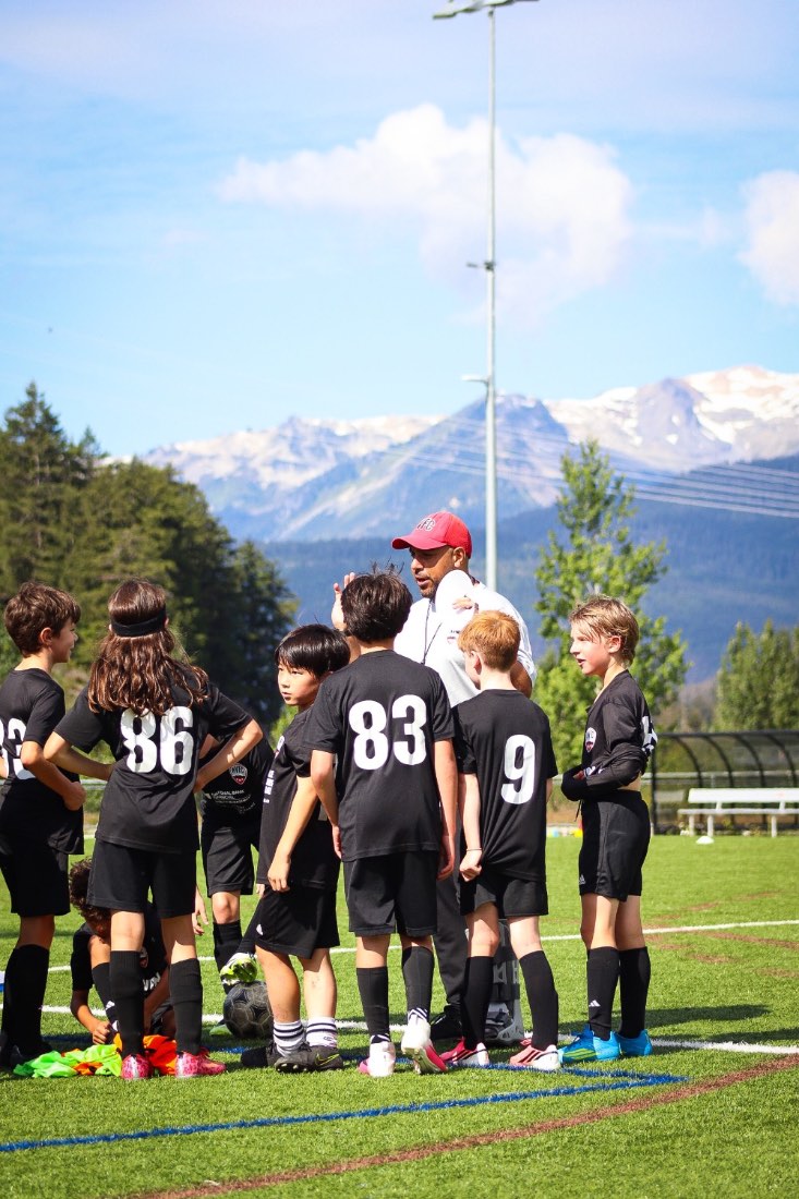 A coach talking to his group, snowy peaks behind